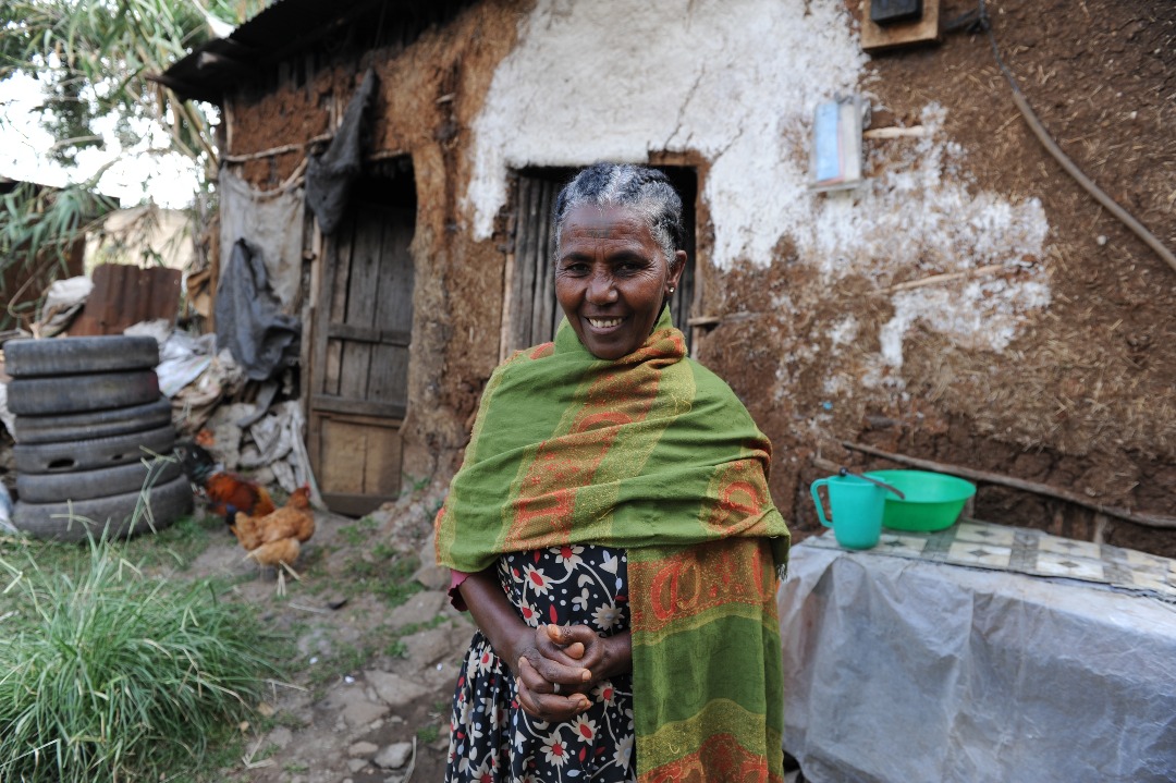 Ethiopian woman standing out the front of her house with chicken coop nearby